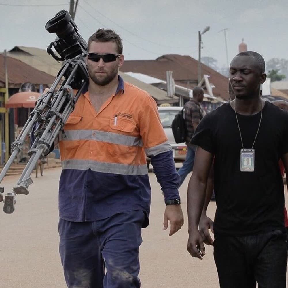 Shawn Peach in hi-vis carrying the camera and tripod in West Africa