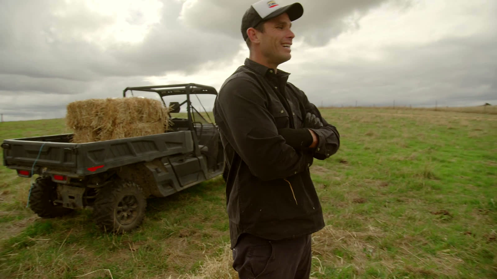 Tom Hawkins, arms folded, beside a Can-Am Defender loaded with hay, a frame from the film