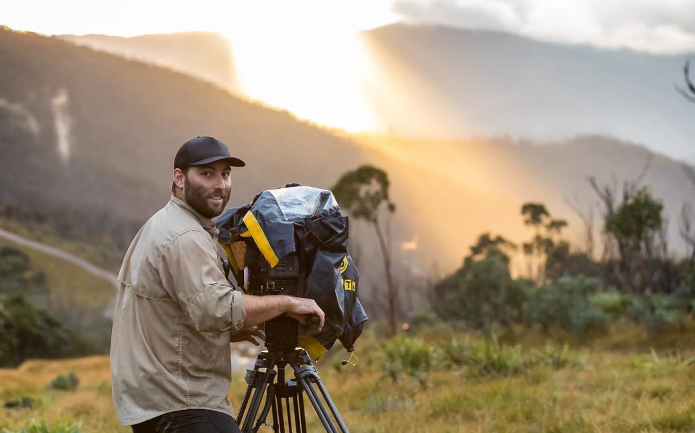 Shawn Peach at the camera on a hillside as the sun breaks through the cloud