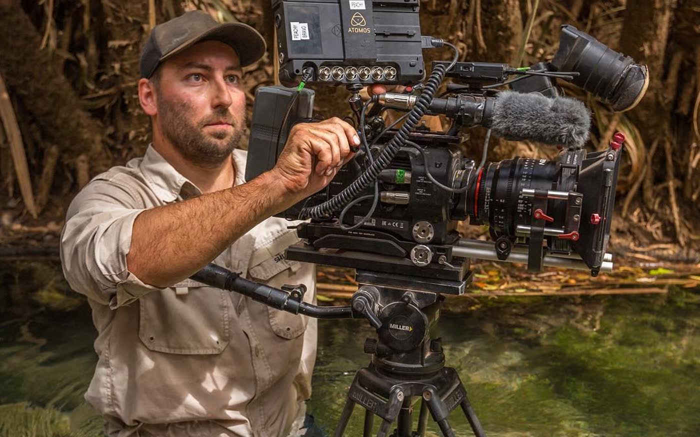 Shawn Peach waist deep in a creek, setting up the camera on a tripod